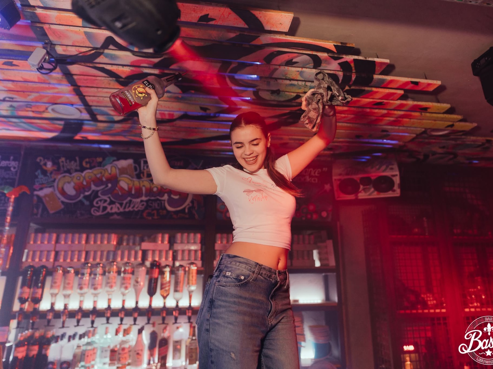 Female staff member partying on the bar under red lights at Bar Bascule